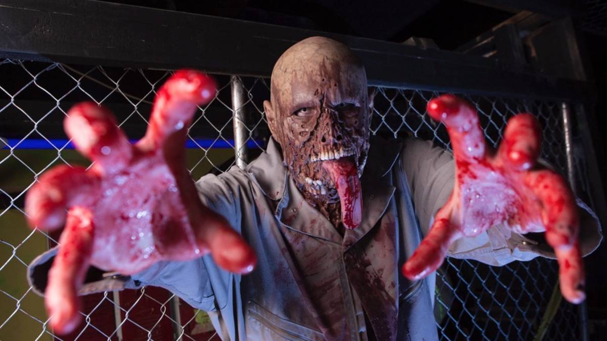 A zombie with bloody hands and a rotting face looking at the camera